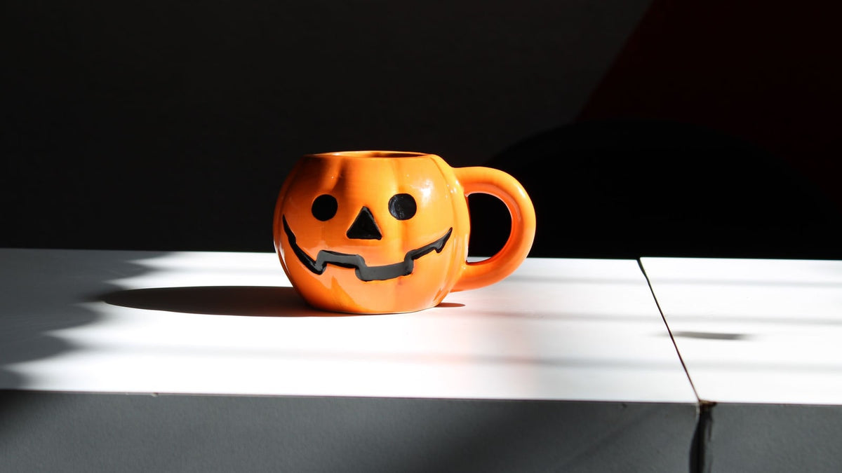 An orange jack-o-lantern mug on a white surface against a dark background