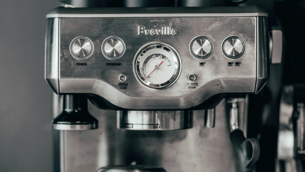 Close-up of a Breville espresso machine with a pressure gauge and coffee tools