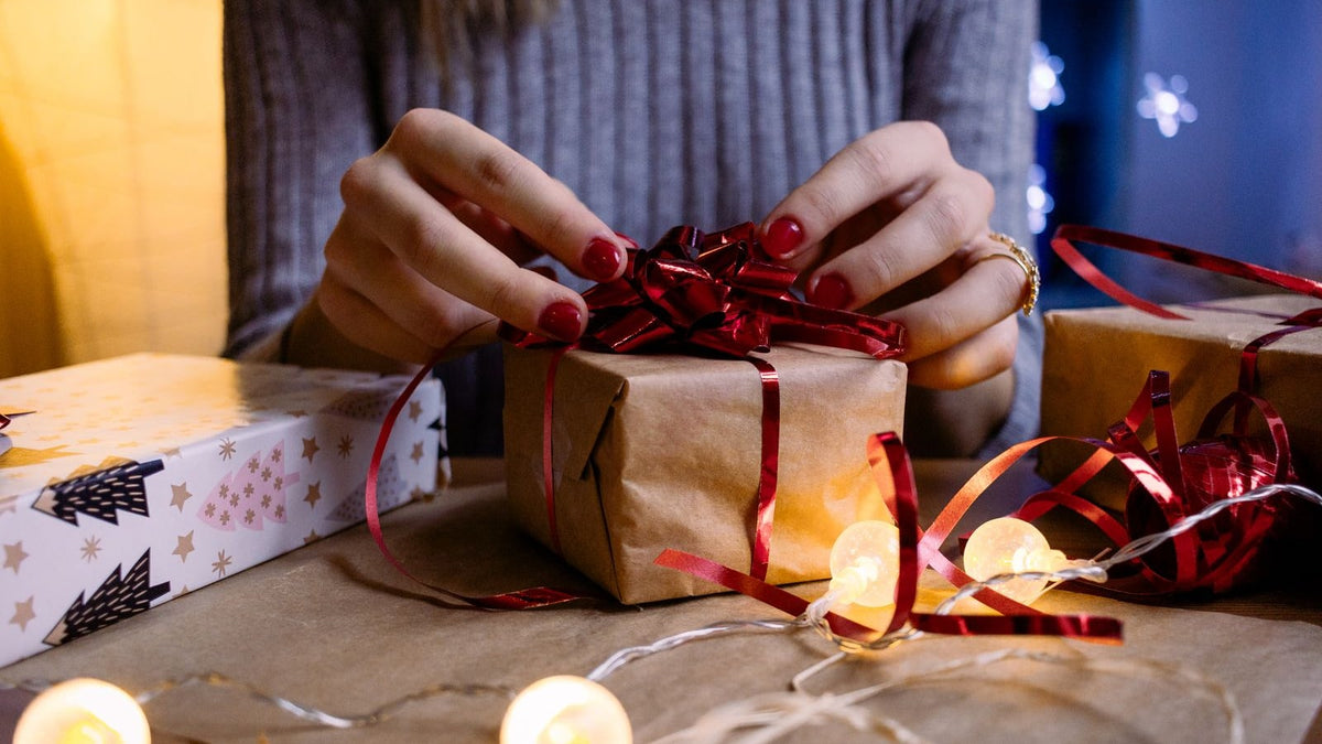 Hands adding a red bow to a wrapped Christmas gift in warm light
