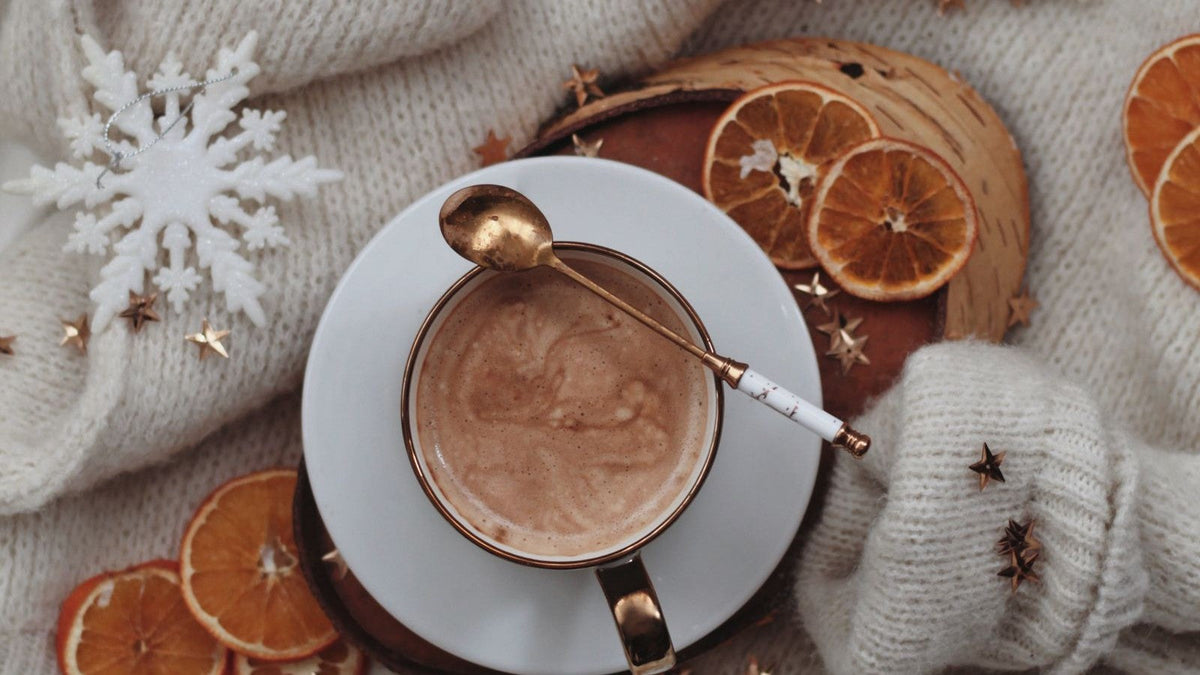 A cup of coffee surrounded by Christmas ornaments and a soft knitted fabric