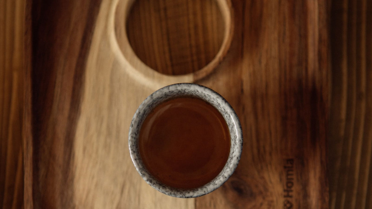Overhead view of a ceramic coffee cup on a tray with contrasting light and dark wood grain