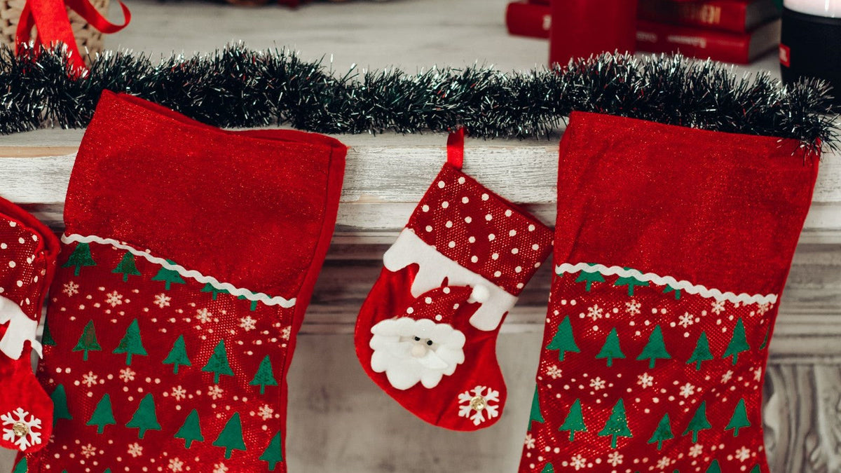 Red Christmas stockings with tree and Santa decorations hanging along a mantel