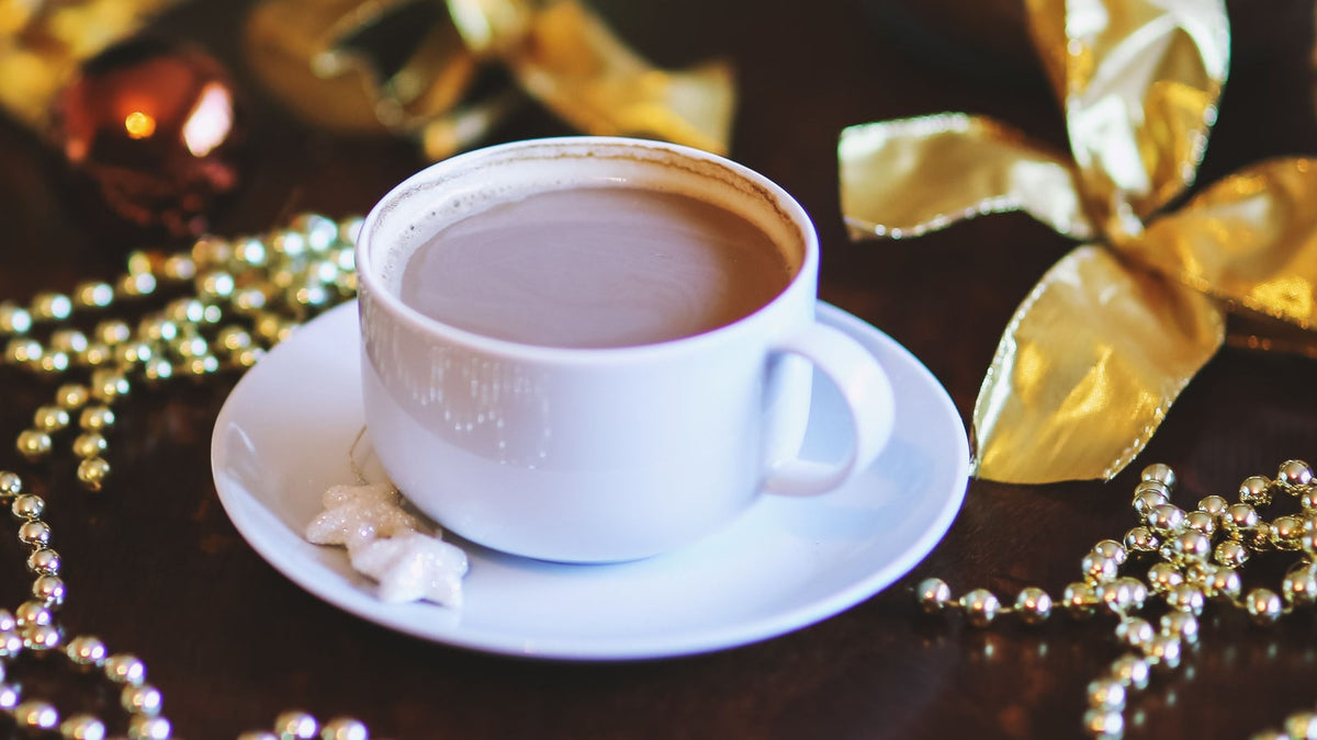 White coffee cup with gold ribbon and Christmas ornaments on a dark tabletop
