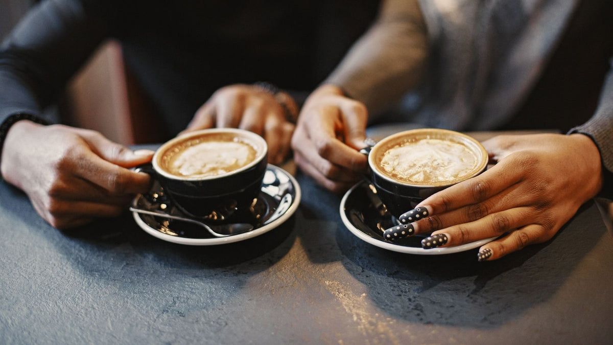 Two people holding black coffee cups and saucers together at a table