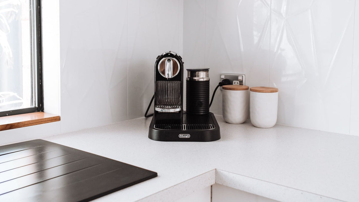Coffee machine and two small canisters on a bright white kitchen corner counter