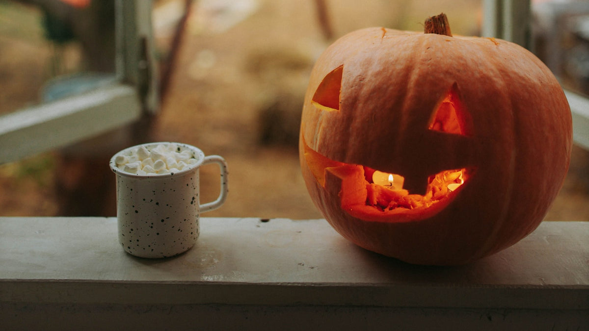 Marshmallow-topped drink beside a glowing jack-o-lantern on a windowsill