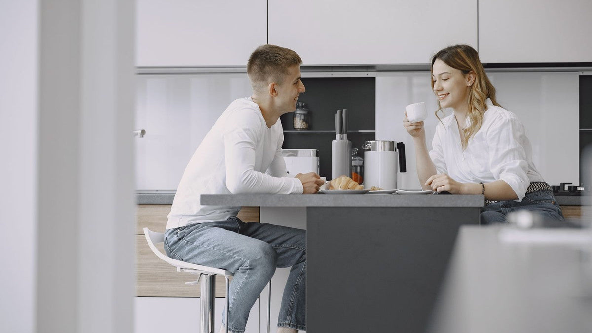 Two people enjoying breakfast and coffee at a kitchen counter