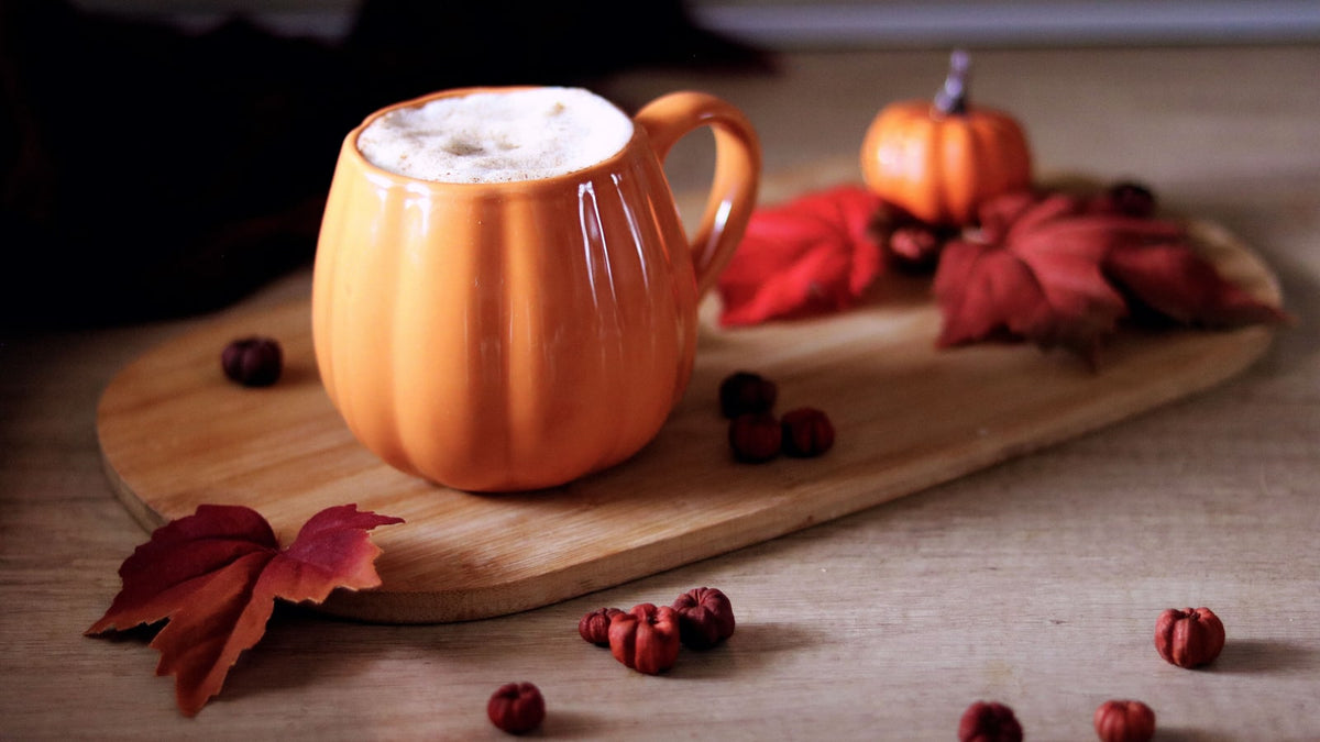 Orange pumpkin-shaped coffee mug on a wooden board with red decorative leaves