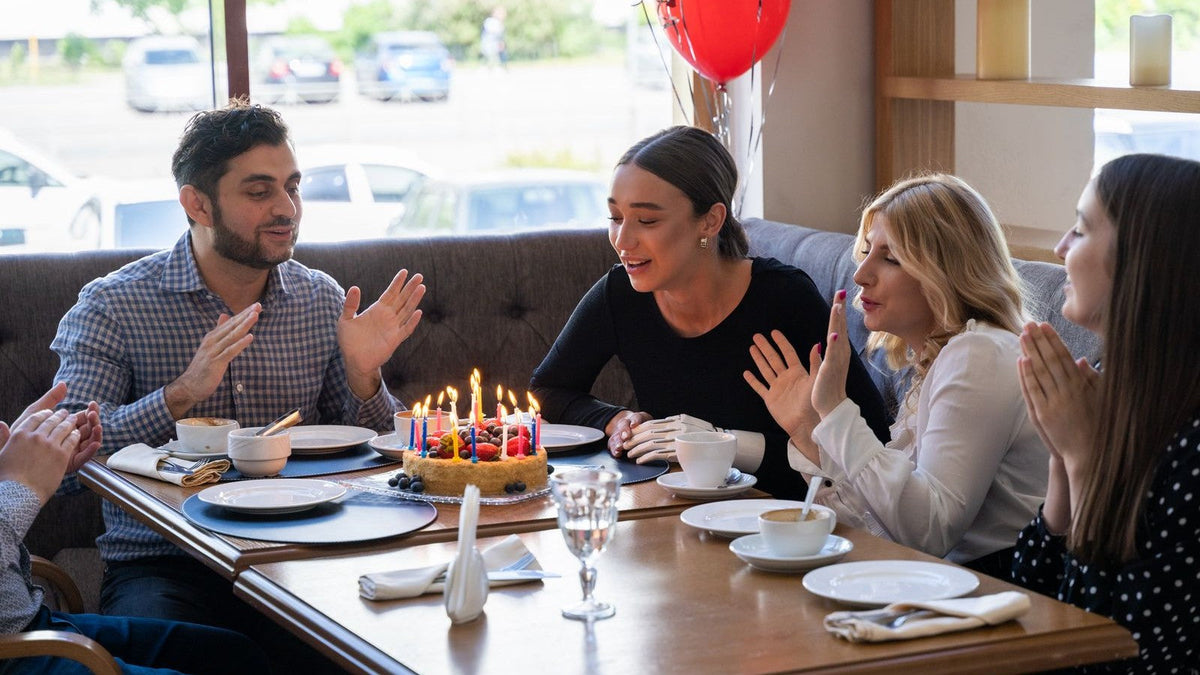 Friends gathered around a birthday cake and coffee cups at a cafe
