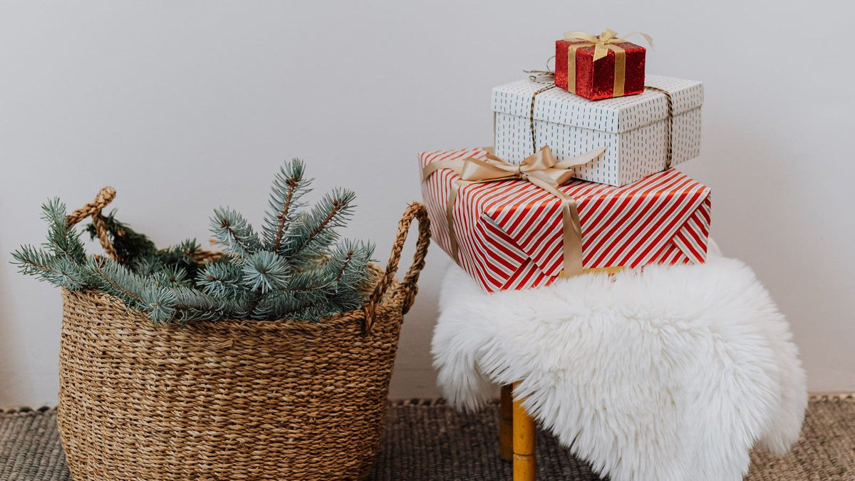 Wrapped Christmas gifts beside a woven basket filled with evergreen branches