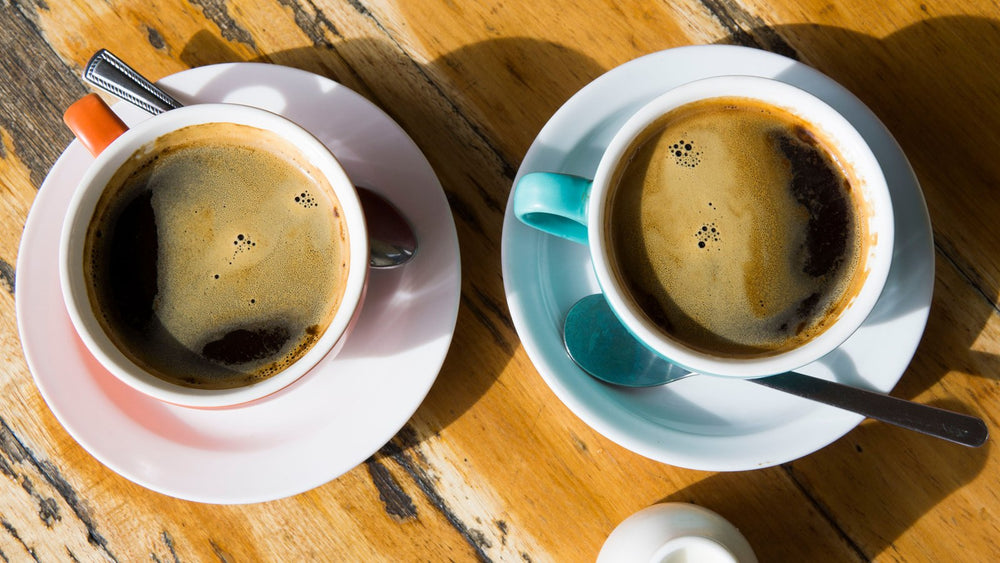 Two cups of black coffee on a wooden café table for drink comparison