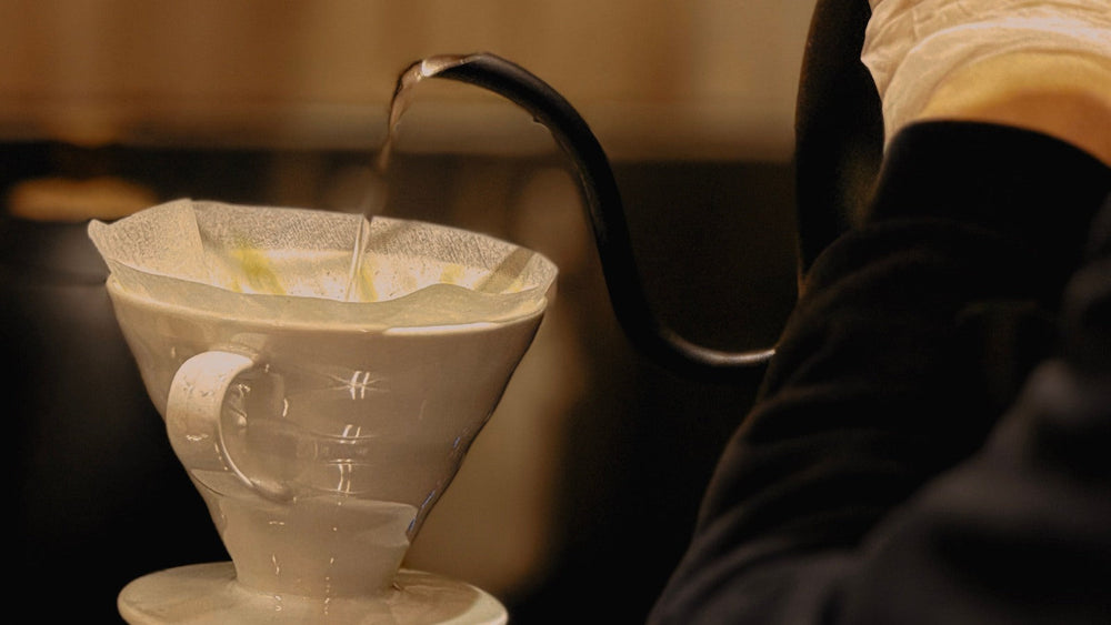 A barista pouring water into a V60-style coffee dripper
