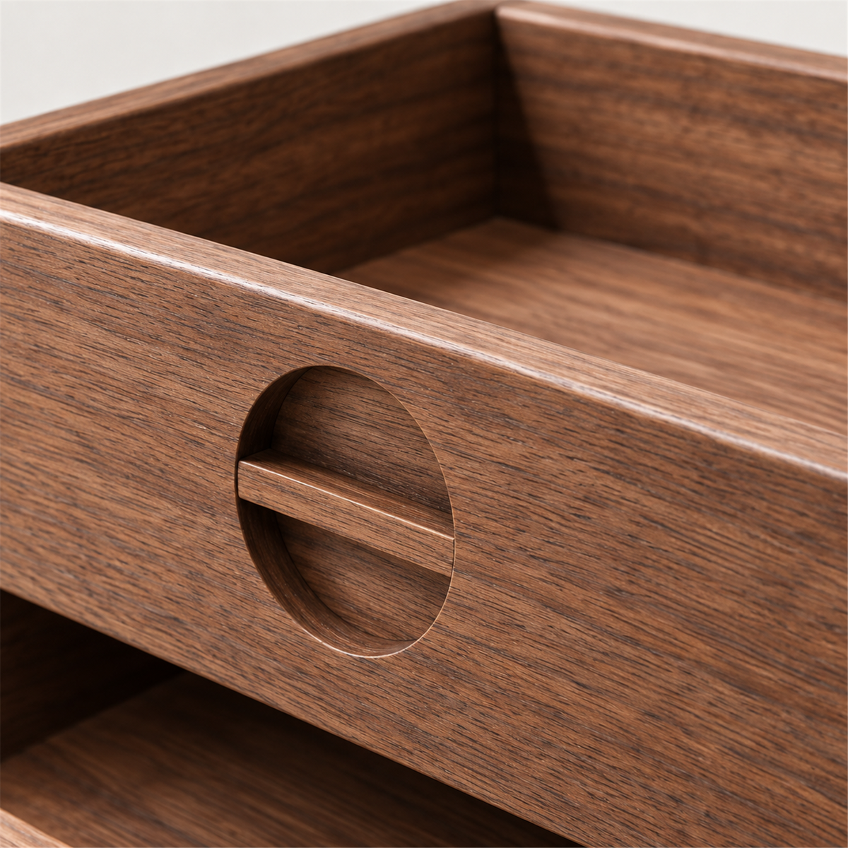 Close-up of the circular recessed finger pull and walnut grain on a tray front