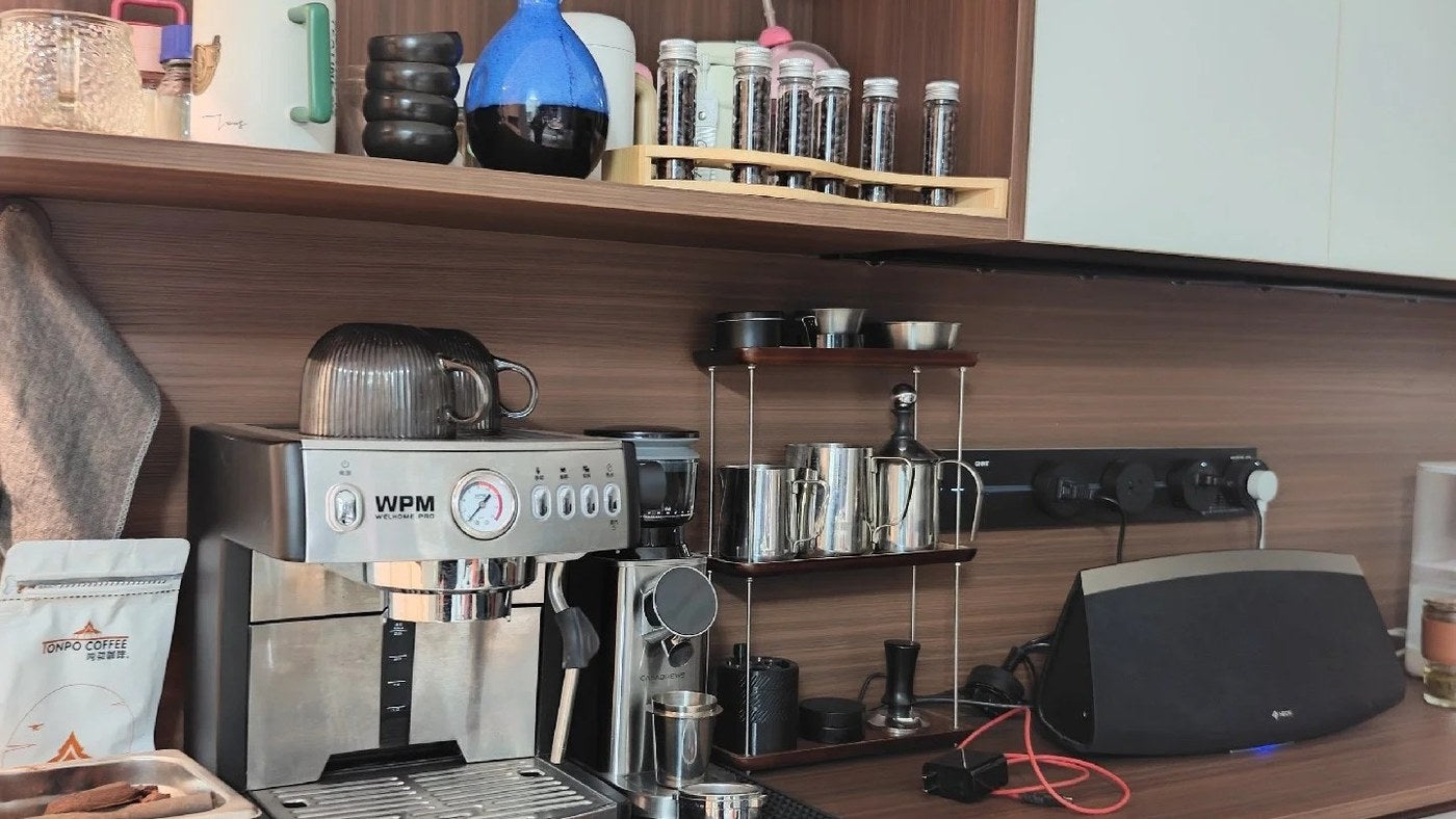 Shared drink station with espresso machine, cups and labeled tea vials on an upper shelf