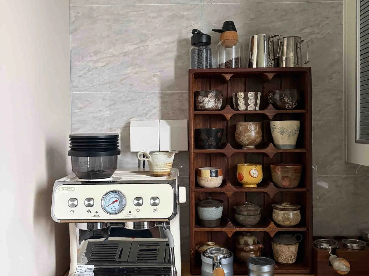 Wood coffee mug cubby rack holding individual ceramic cups beside an espresso machine