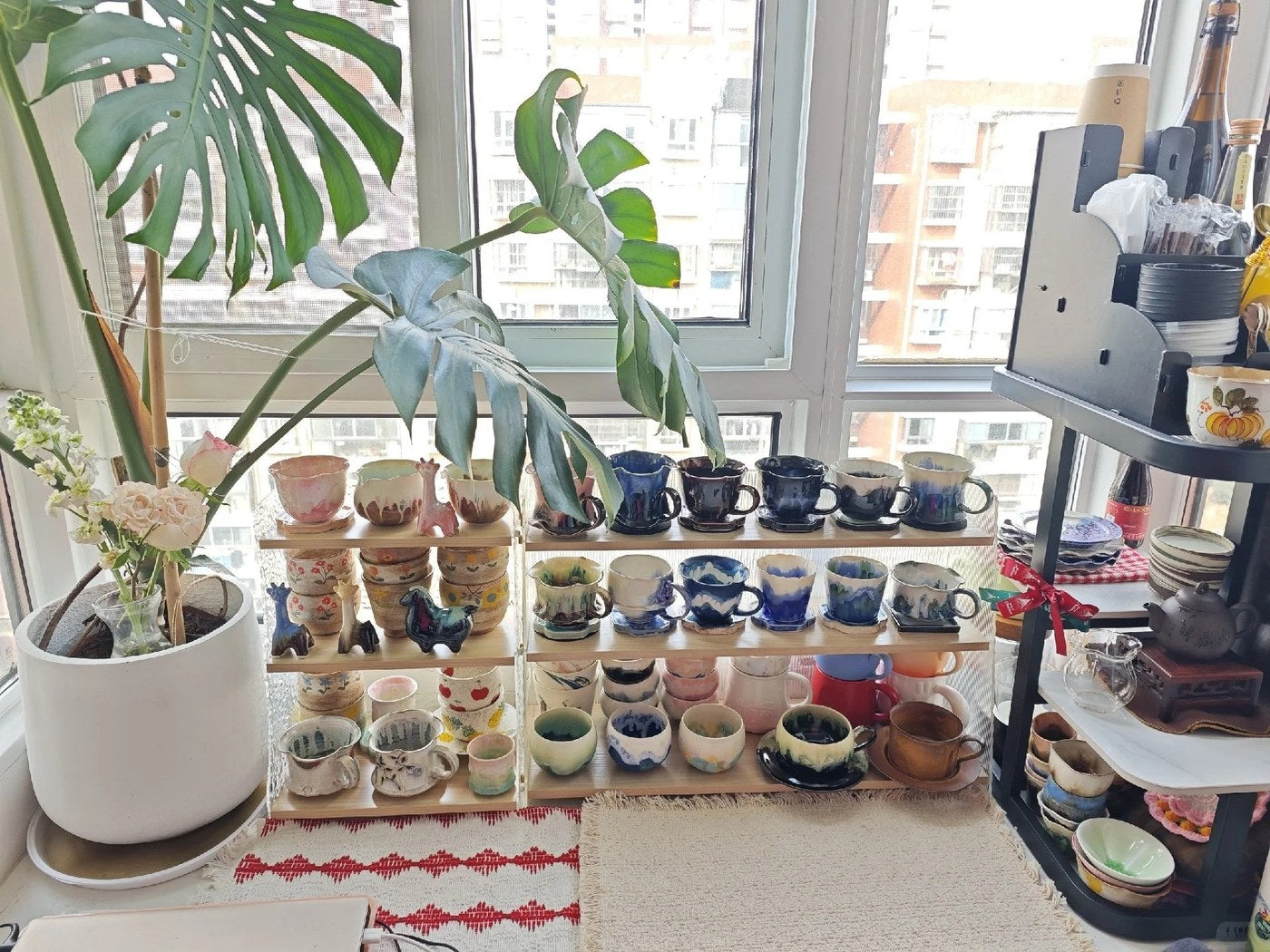 Handmade coffee cups grouped in blue, pink, cream and earth-tone families beneath a large green plant